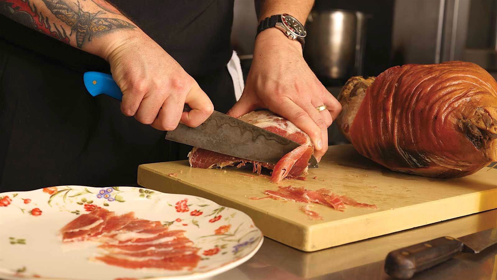 A chef at Holly Hill slices a ham thinly in the kitchen.